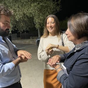 Group tasting freshly pressed extra-virgin olive oil outside an olive mill in Chiaramonte, Sicily, smiling and warming the oil between hands.