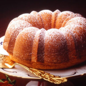Golden bundt-style olive oil cake dusted with powdered sugar, served on an ornate cakestand.